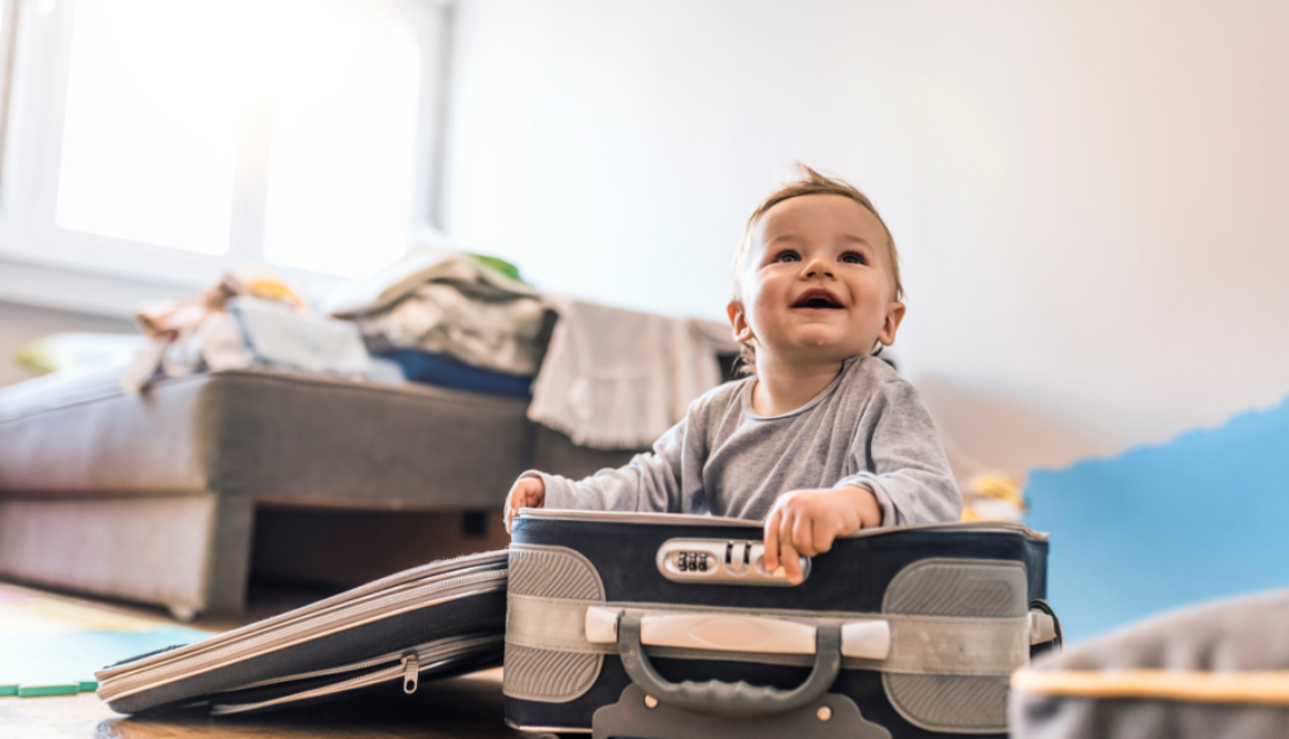 A baby smiling while sitting inside an open suitcase.