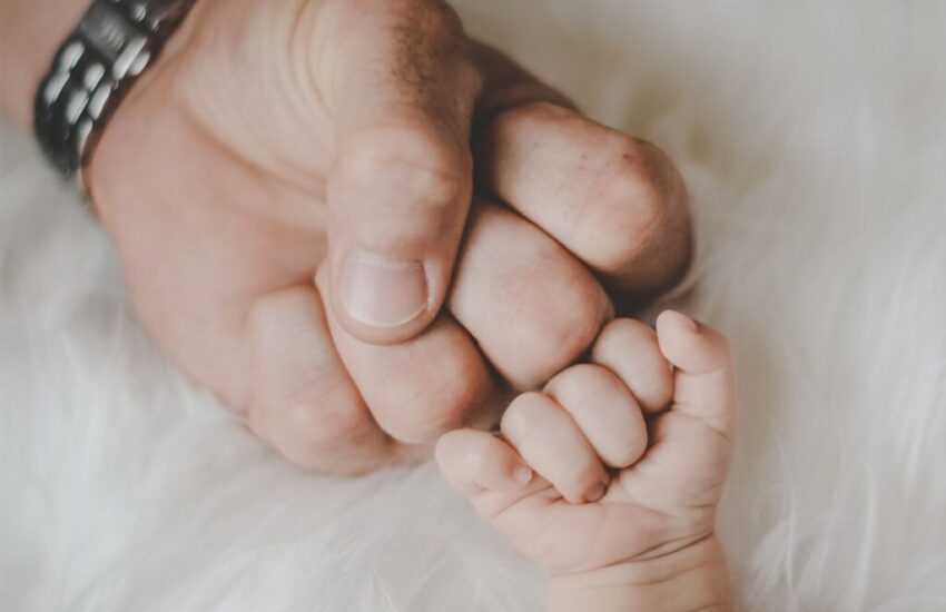 A remembrance photo of the father and child's hands together after the baby is born.
