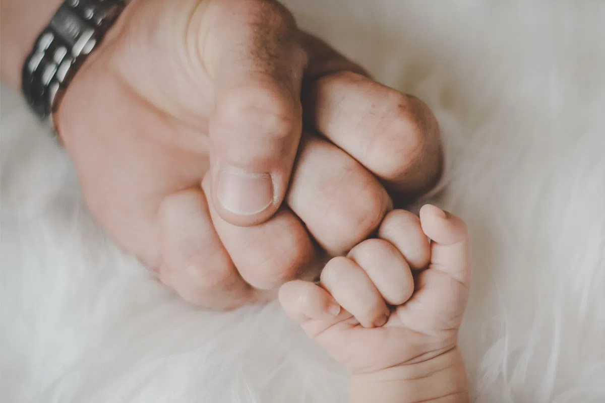 A remembrance photo of the father and child's hands together after the baby is born.